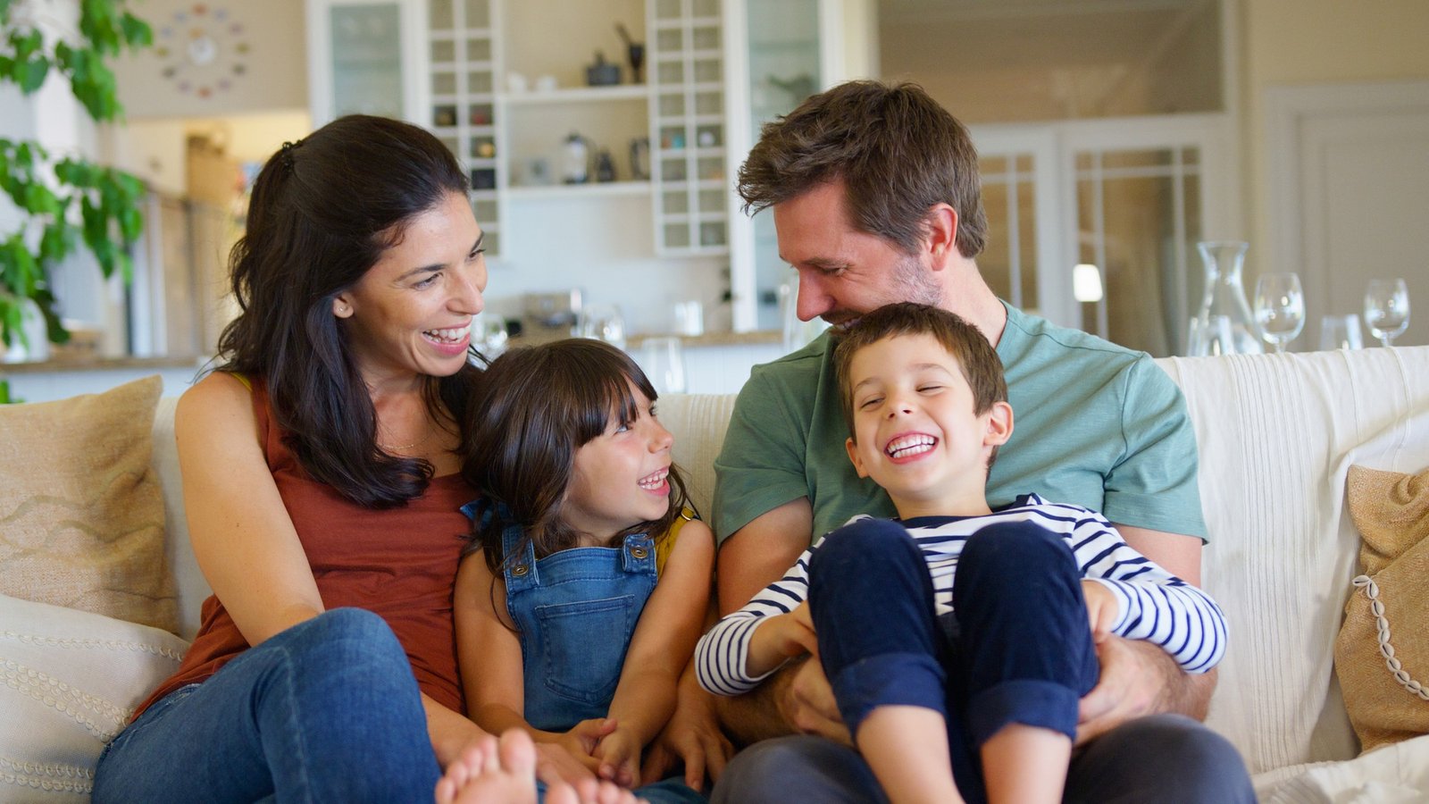 Smiling Family Sitting With On Sofa At Home Laughing Together